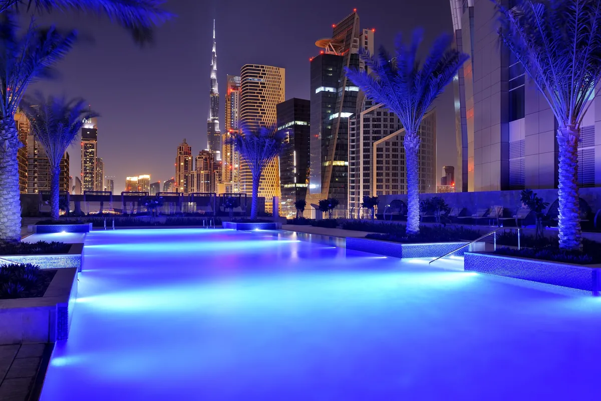 JW Marriott Marquis Hotel Dubai: A nighttime view of a modern cityscape with illuminated buildings and a pool area.